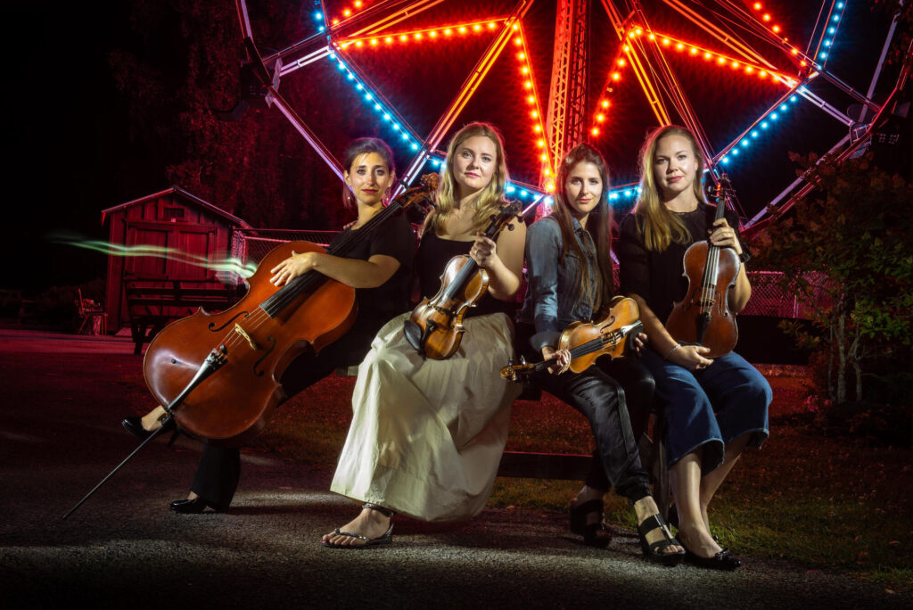 ATLYS posing with their instruments in front of a lit-up Ferris wheel at night